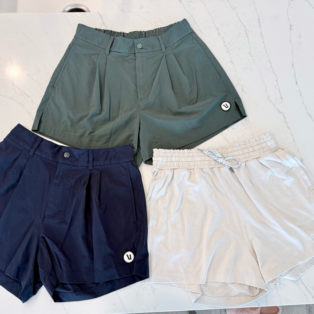 3 Pairs of Vuori Women's Athletic Shorts - Hunter Green, Navy, and Cream.